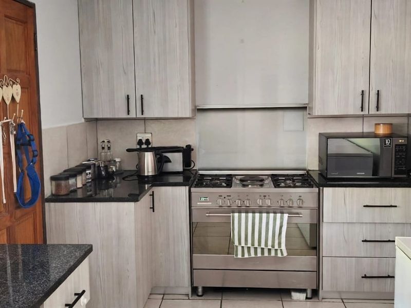 A functional kitchen featuring light wood-grain cabinetry, dark granite countertops, a gas stove with extractor fan, and neutral tiled flooring.