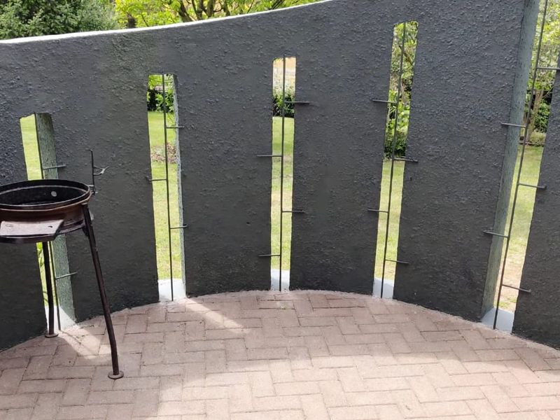 A private outdoor patio area featuring a unique curved masonry wall with vertical metal detailing and paved flooring, overlooking a garden space.