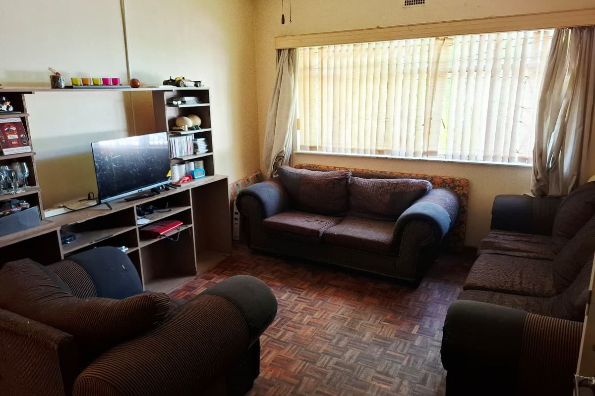 A living room featuring original parquet flooring and large windows with vertical blinds, offering a dated interior space ready for modernization.