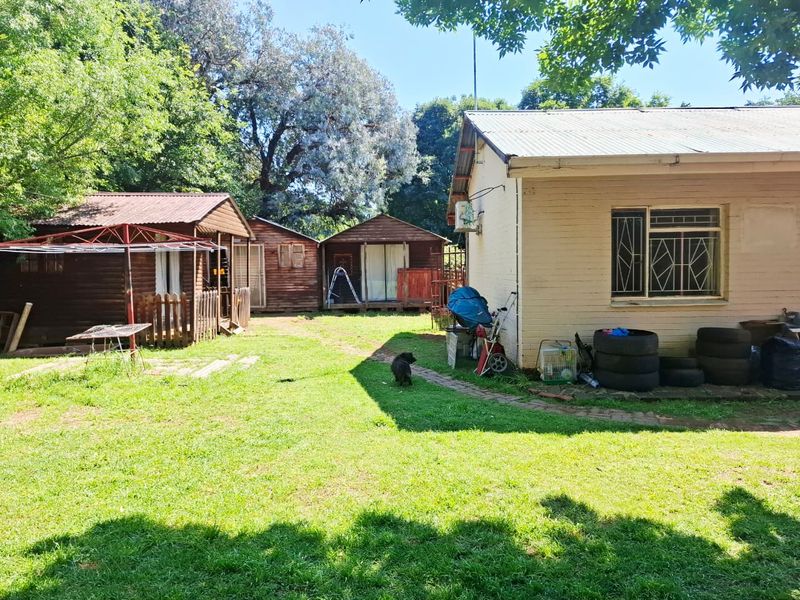 Rear garden view featuring multiple timber outbuildings and the rear elevation of the main house with security-barred windows and corrugated roofing.