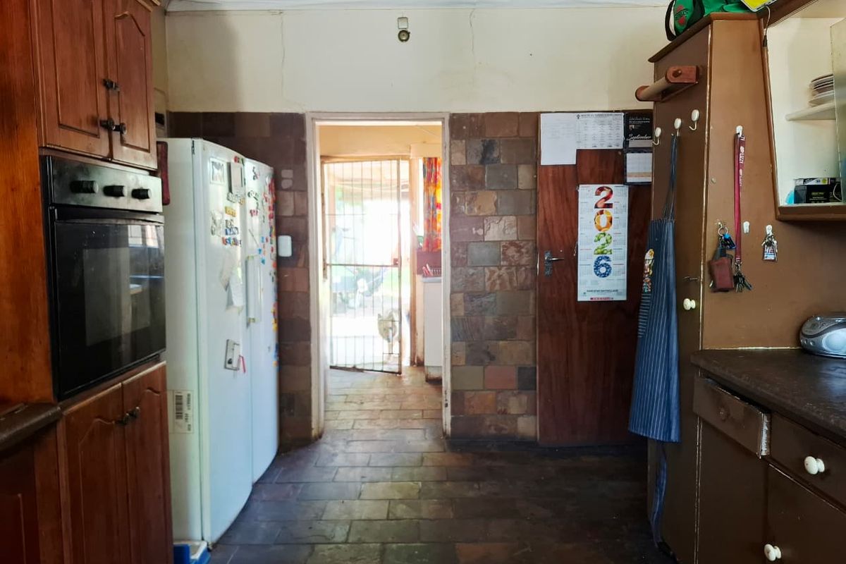 A dated kitchen featuring wooden cabinetry, stone tile flooring, and stone wall cladding, leading through to an exterior doorway with a security gate.