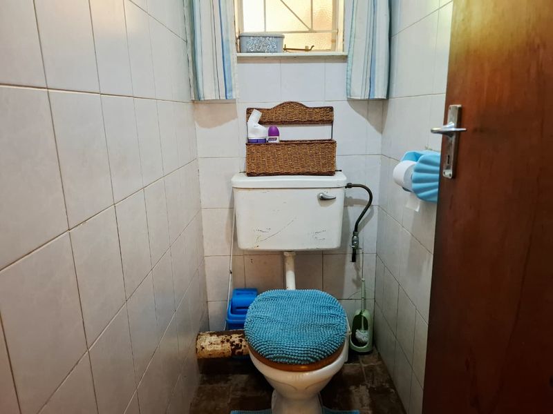A compact bathroom featuring full-height ceramic wall tiling and a standard toilet suite, currently showing signs of age and wear.