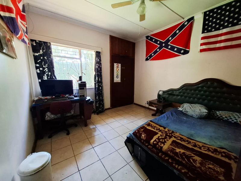 A bedroom featuring tiled flooring, a ceiling fan, and a built-in cupboard, with security bars installed on the window.
