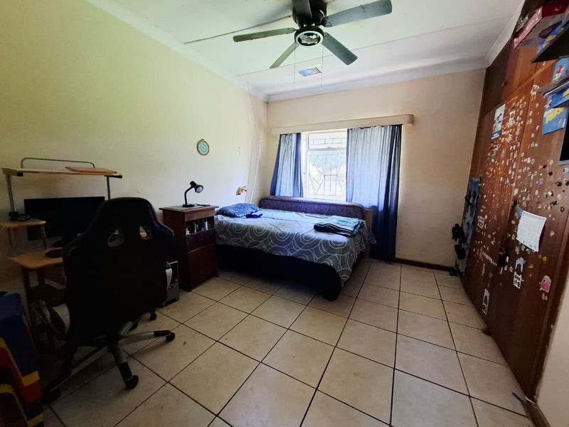 A bedroom featuring tiled flooring, a ceiling fan, and built-in cupboards with security bars on the window.