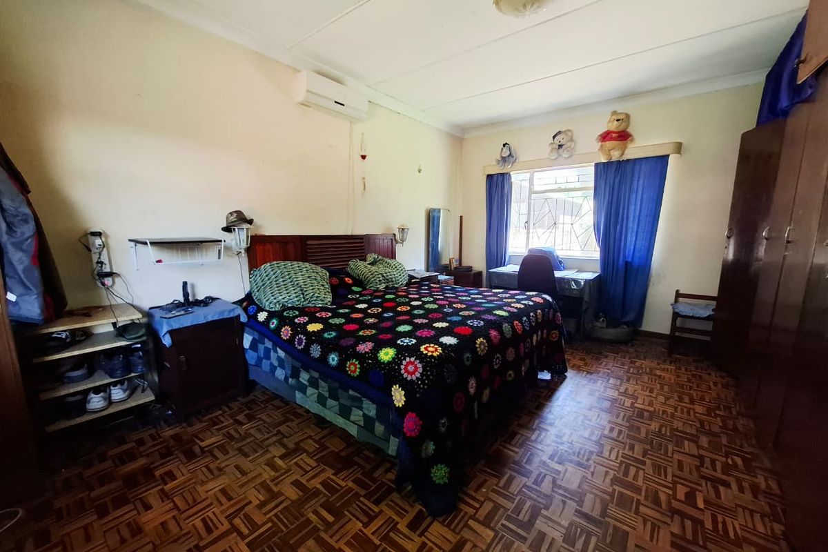 A spacious bedroom featuring traditional parquet flooring, built-in cupboards, and a wall-mounted air conditioning unit, offering a functional layout with potential for modernization.