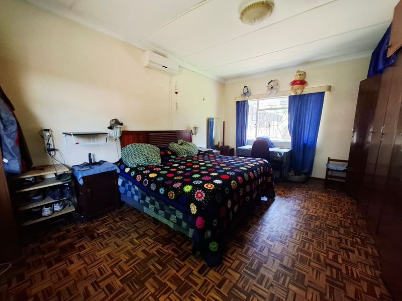 A spacious bedroom featuring traditional parquet flooring, built-in cupboards, and a wall-mounted air conditioning unit, offering a functional layout with potential for modernization.