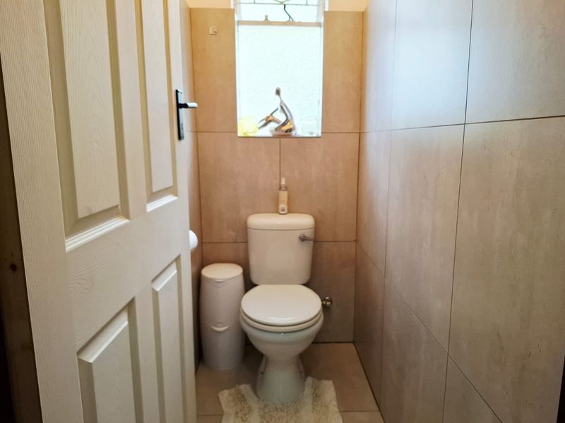 A compact, well-maintained bathroom featuring neutral wall and floor tiling, a standard toilet, and a small window for natural light.