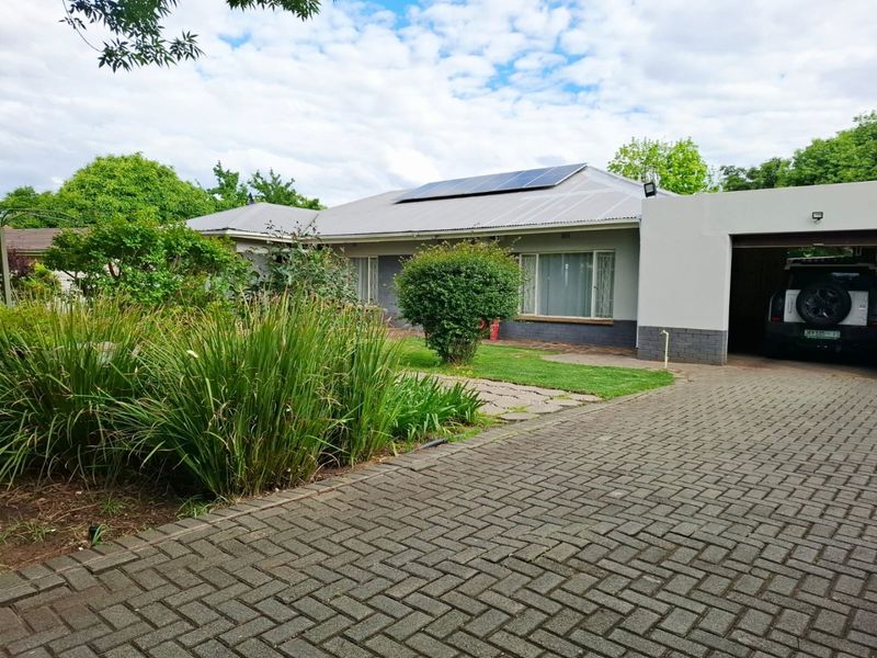 Front view of a single-story house featuring a paved driveway, attached garage, and roof-mounted solar panels set within a landscaped garden.