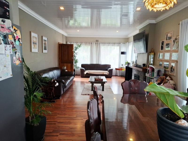 Spacious open-plan living and dining area featuring warm laminate flooring, a stone-clad fireplace, and a modern glossy ceiling with recessed lighting.