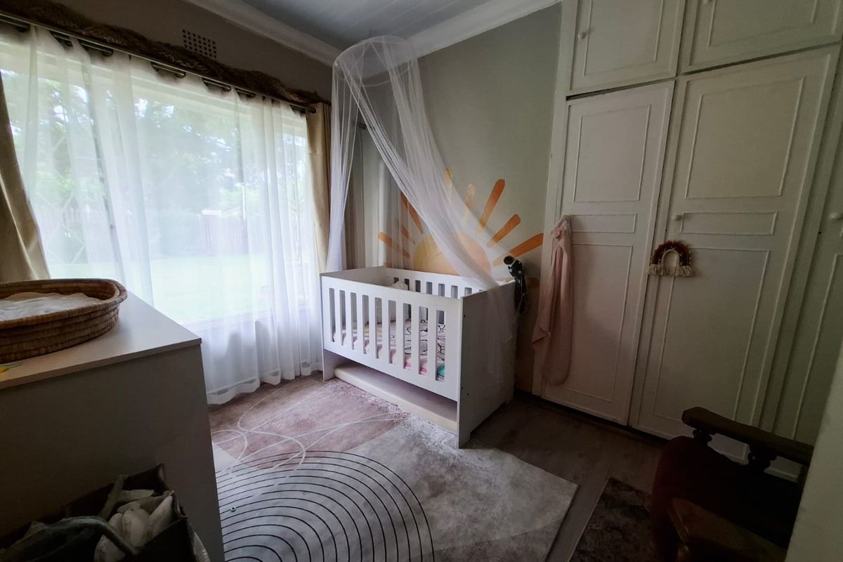 A bedroom featuring built-in cupboards, large window with natural light, and neutral flooring, currently styled as a nursery.