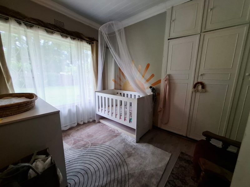 A bedroom featuring built-in cupboards, large window with natural light, and neutral flooring, currently styled as a nursery.