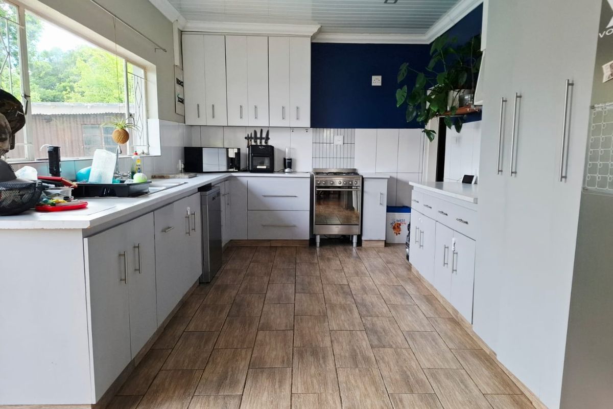 A functional kitchen featuring light grey cabinetry, wood-look tiled flooring, a stainless steel oven, and a bright, clean layout with ample counter space.