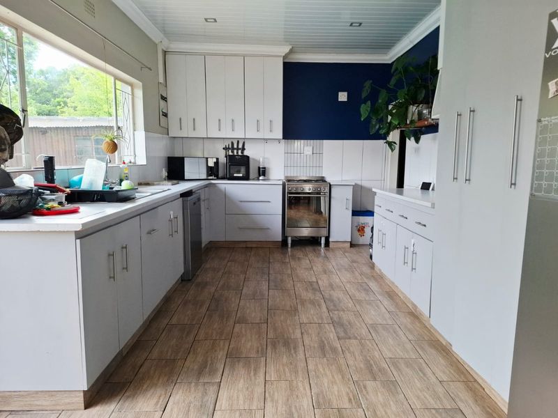A functional kitchen featuring light grey cabinetry, wood-look tiled flooring, a stainless steel oven, and a bright, clean layout with ample counter space.