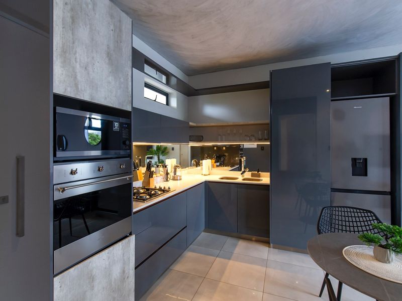 Modern kitchen featuring sleek grey cabinetry, stone countertops, integrated appliances, a gas hob, and a stylish mirrored splashback.