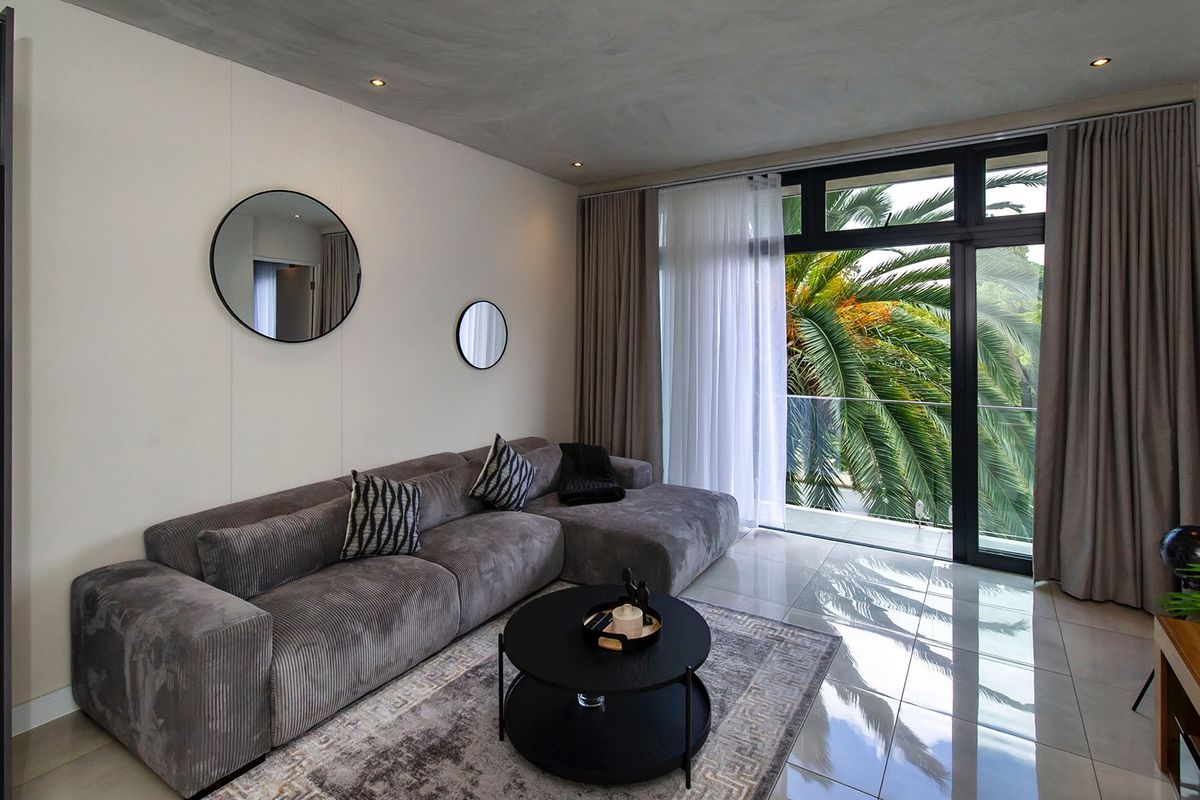 Modern living room featuring tiled floors, recessed lighting, and large sliding glass doors opening to a balcony with lush greenery views.