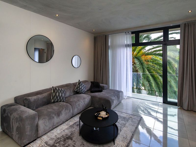 Modern living room featuring tiled floors, recessed lighting, and large sliding glass doors opening to a balcony with lush greenery views.