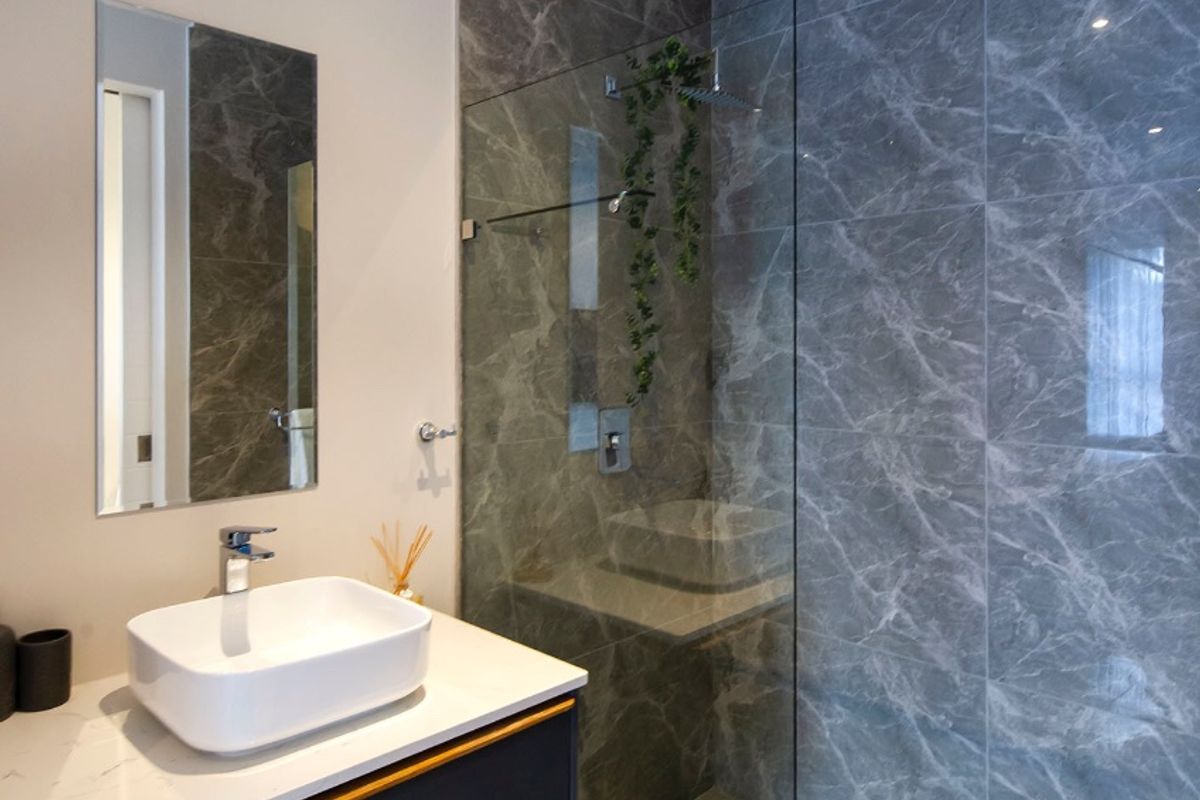Modern bathroom featuring a sleek vessel sink on a stone vanity, complemented by a spacious walk-in shower with elegant marble-effect wall tiling.