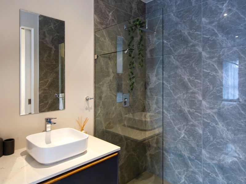 Modern bathroom featuring a sleek vessel sink on a stone vanity, complemented by a spacious walk-in shower with elegant marble-effect wall tiling.