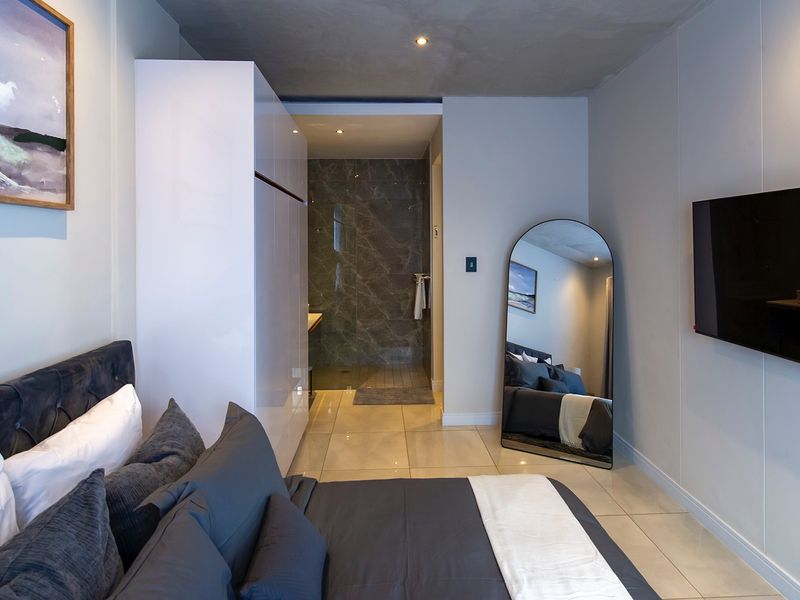 Modern bedroom featuring tiled flooring, recessed lighting, a sleek built-in wardrobe, and direct access to a contemporary en-suite bathroom.