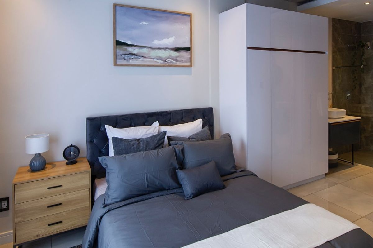 A modern bedroom featuring a built-in wardrobe, recessed lighting, and tiled flooring, with direct access to an en-suite bathroom.