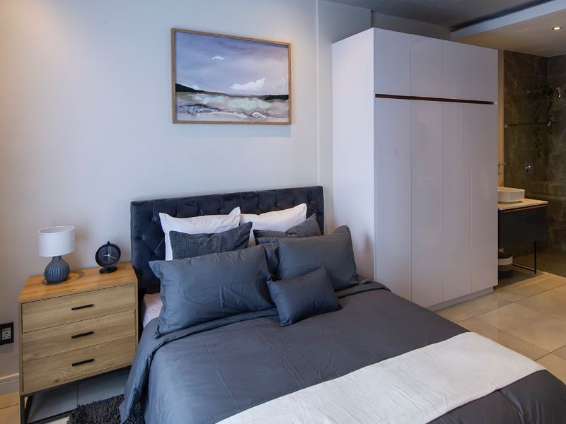 A modern bedroom featuring a built-in wardrobe, recessed lighting, and tiled flooring, with direct access to an en-suite bathroom.