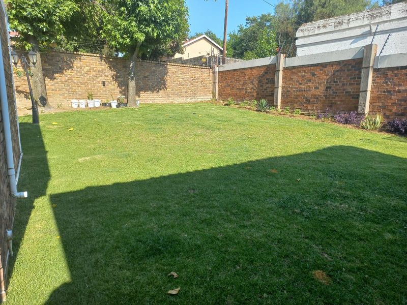 A private rear garden featuring a well-maintained lawn enclosed by secure brick boundary walls with integrated electric fencing.