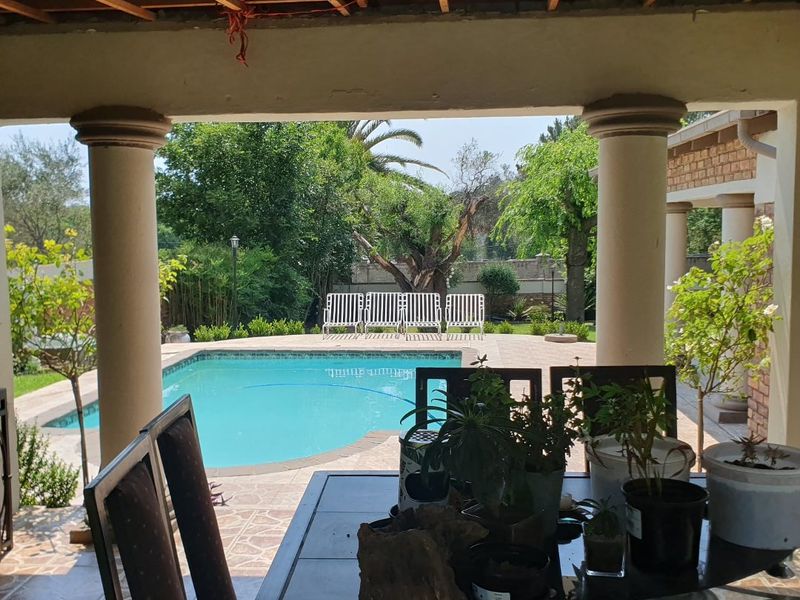 Covered patio area featuring tiled flooring and concrete columns, overlooking a swimming pool and garden space.