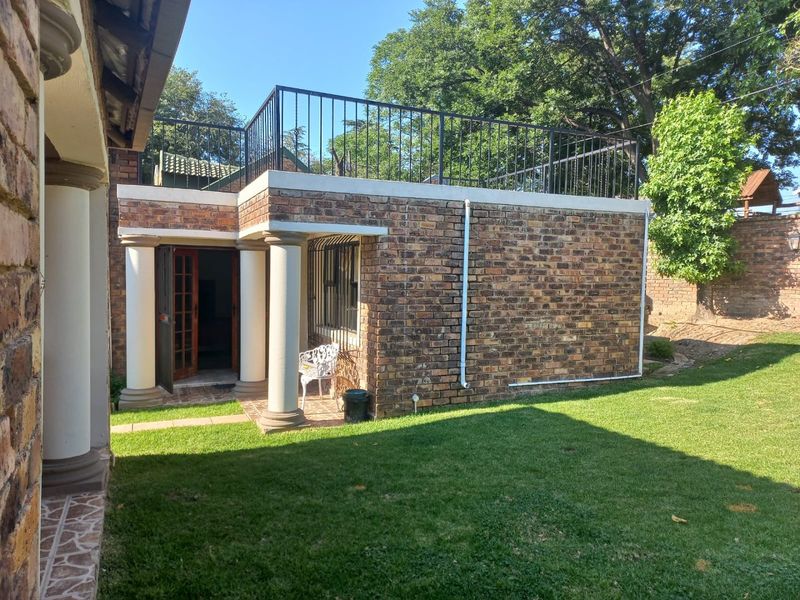 Rear view of the property featuring a face brick facade, classical columns, and an accessible roof terrace with a metal balustrade overlooking the garden.