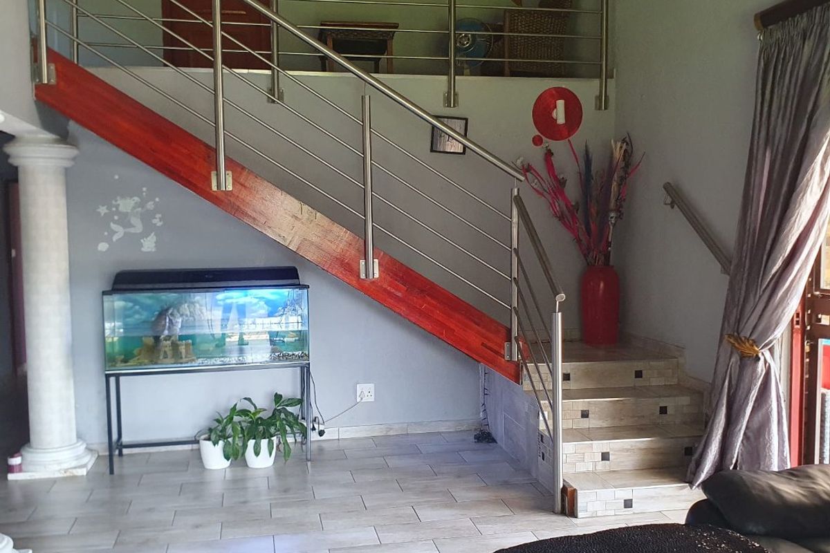 Living area featuring a timber staircase with stainless steel balustrade, tiled flooring, and exposed timber rafters leading to a mezzanine level.