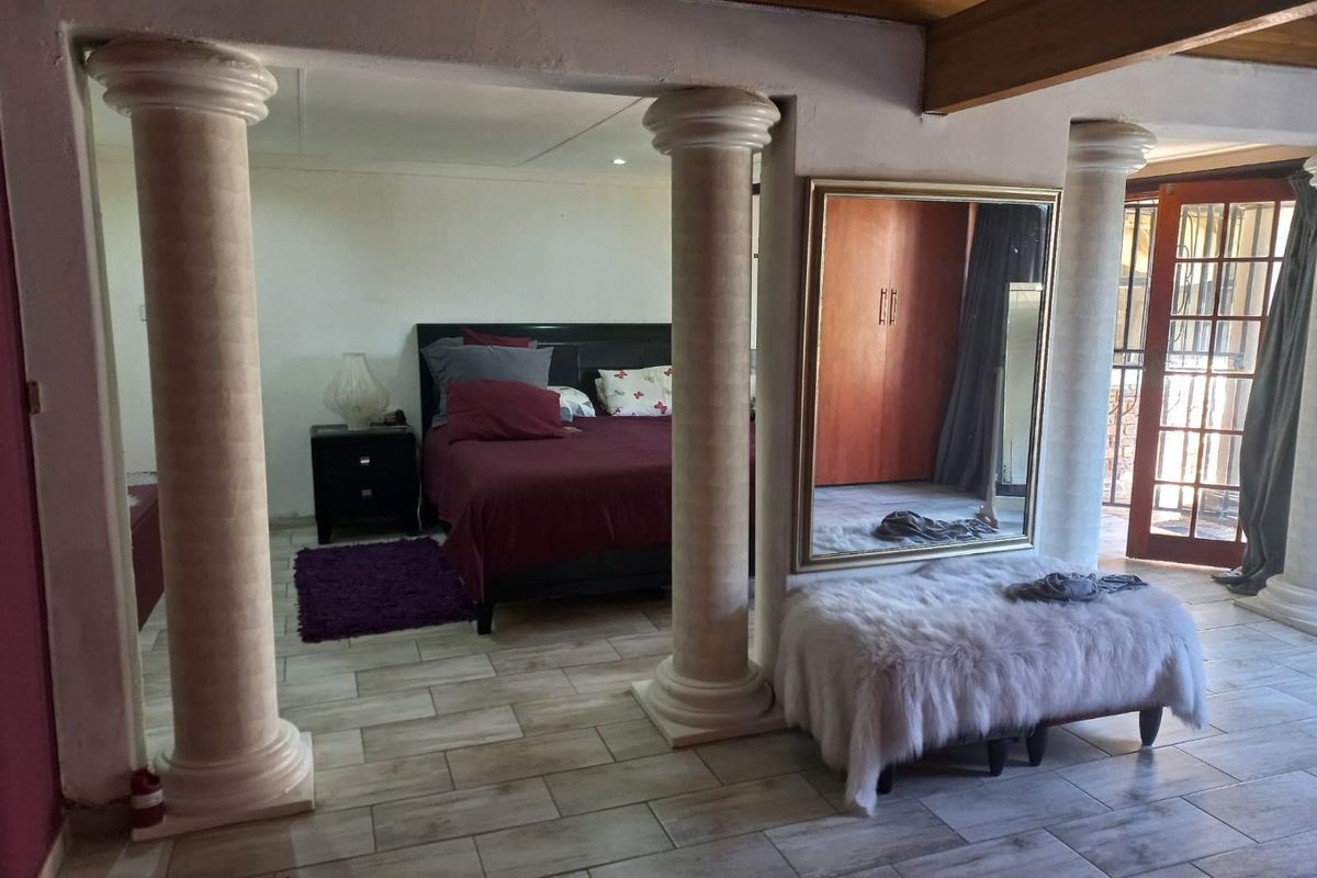 Spacious bedroom featuring decorative columns, exposed timber ceiling beams, tiled flooring, and a built-in wardrobe with direct access to an outdoor area.