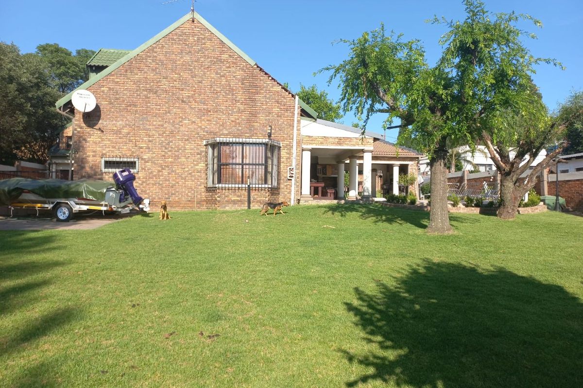 Rear view of a face brick house featuring a spacious lawn and a covered patio area.