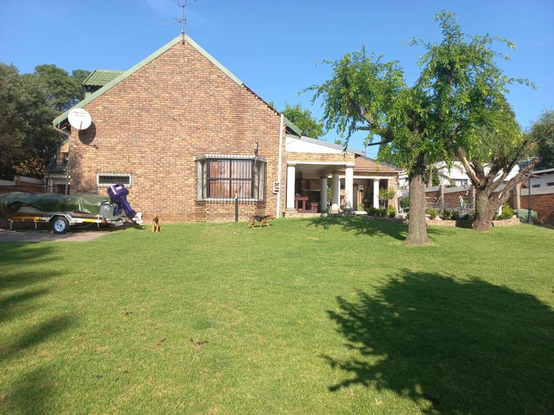 Rear view of a face brick house featuring a spacious lawn and a covered patio area.