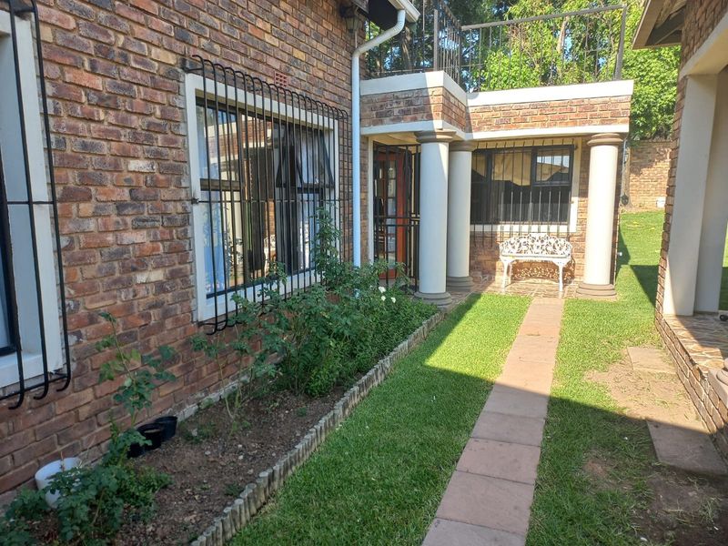 Rear exterior view of a face brick house featuring a paved walkway, garden area, and a balcony with metal railings.