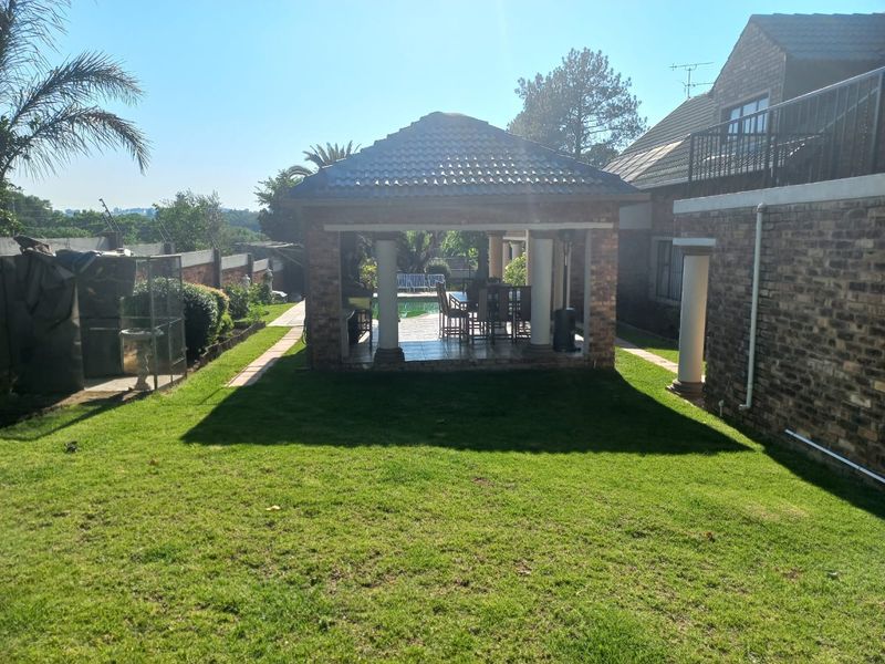 A spacious rear garden featuring a covered brick gazebo with stone columns, overlooking a well-maintained lawn and the main house structure.