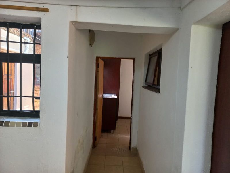 A narrow interior hallway featuring tiled flooring, security bars on the window, and timber door frames, showing signs of wear and wall staining.
