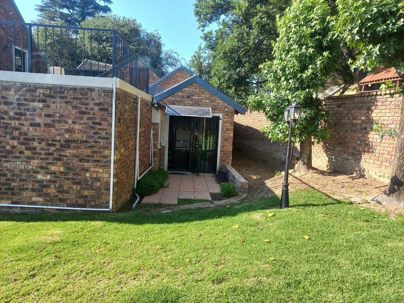 Rear exterior view featuring a brick facade, paved walkway, garden area, and a metal security gate leading to the entrance.