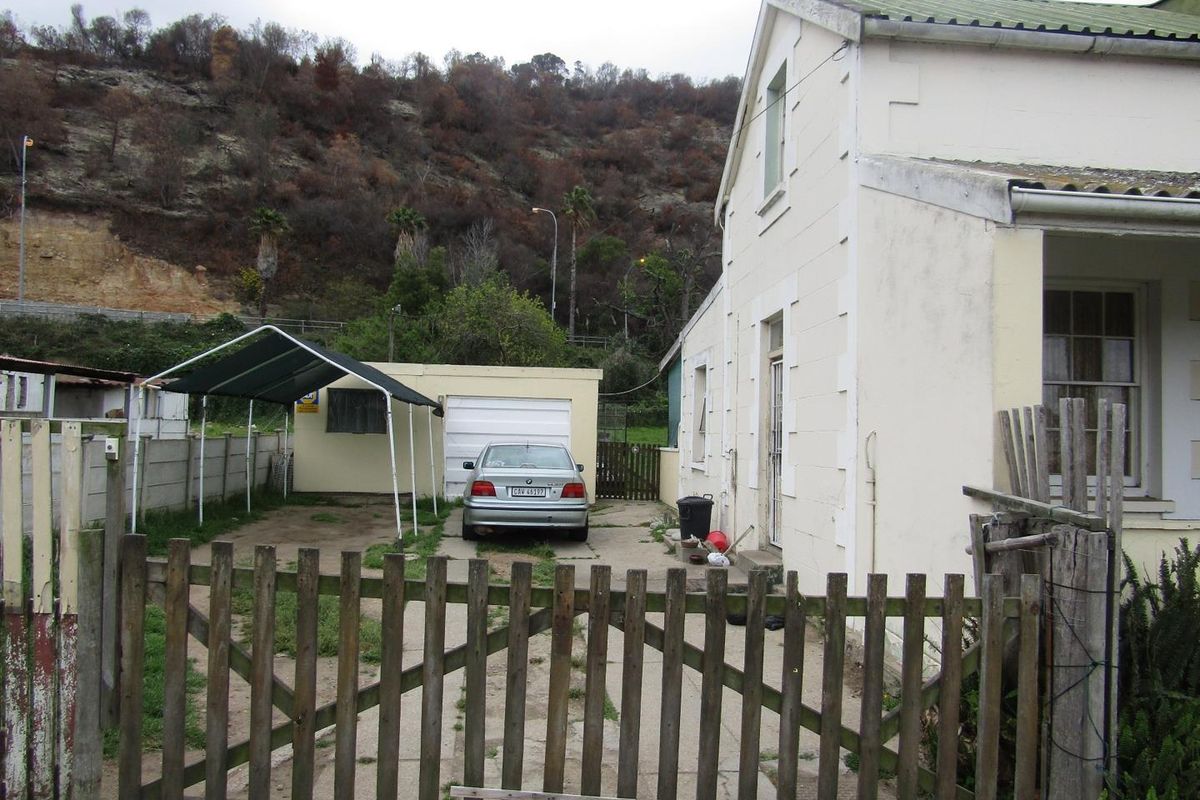 Rear exterior view of the property featuring a concrete driveway, single garage, carport, and timber fencing against a hillside backdrop.
