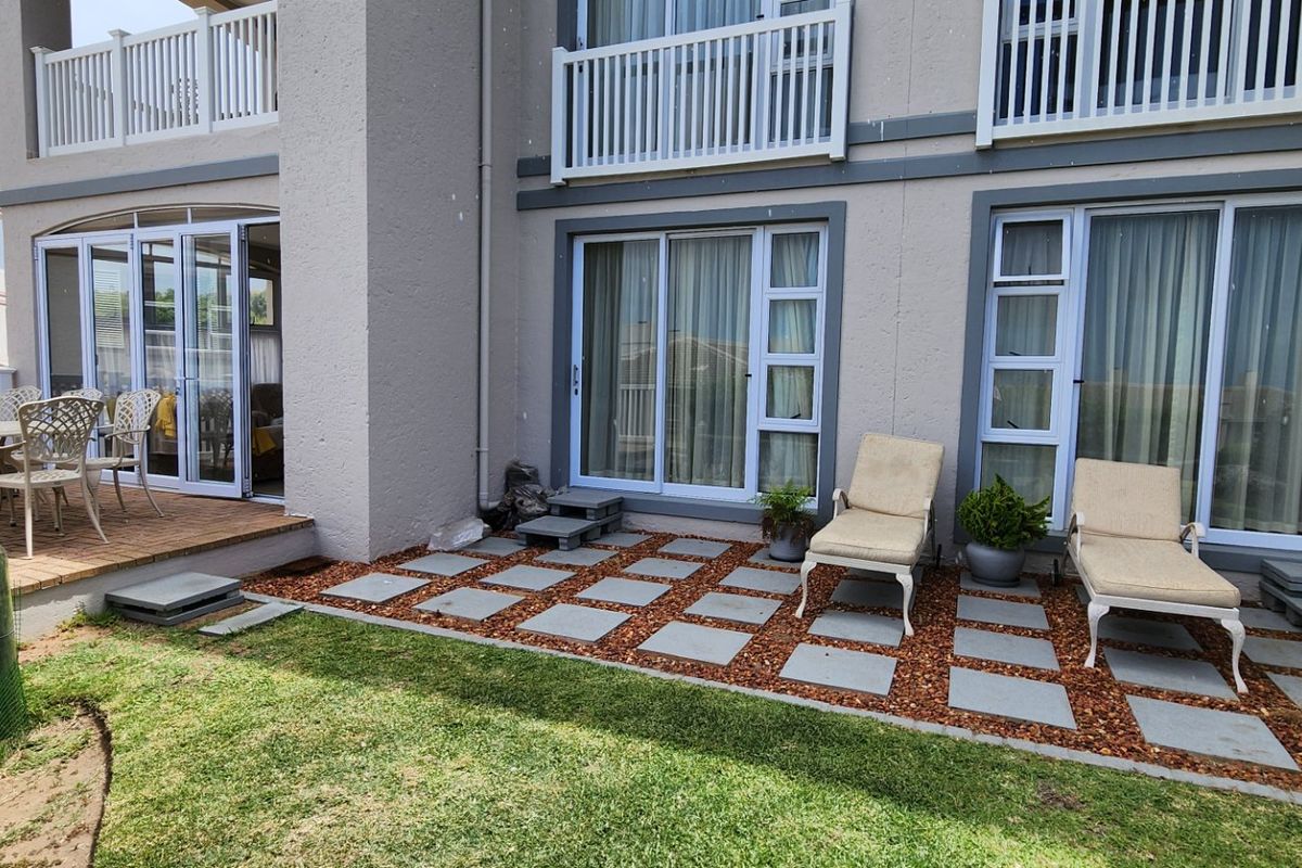 A well-maintained rear exterior featuring a paved patio area, timber decking, and multiple sliding glass door access points to the apartment interior.