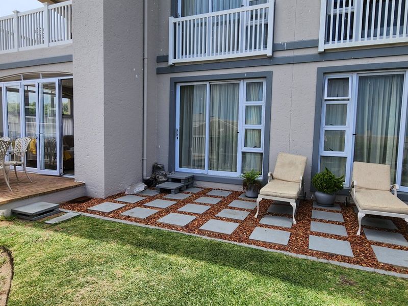 A well-maintained rear exterior featuring a paved patio area, timber decking, and multiple sliding glass door access points to the apartment interior.