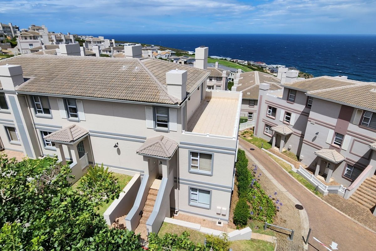 Aerial view of a residential apartment complex featuring tiled roofs, paved driveways, and coastal views.