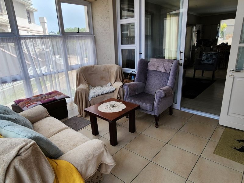A bright, enclosed patio or sunroom featuring tiled flooring, large windows, and sliding glass door access to the main living area.