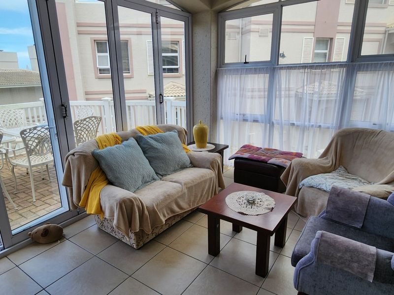 An enclosed balcony or sunroom featuring tiled flooring and large aluminium sliding doors that provide ample natural light and access to an outdoor patio area.