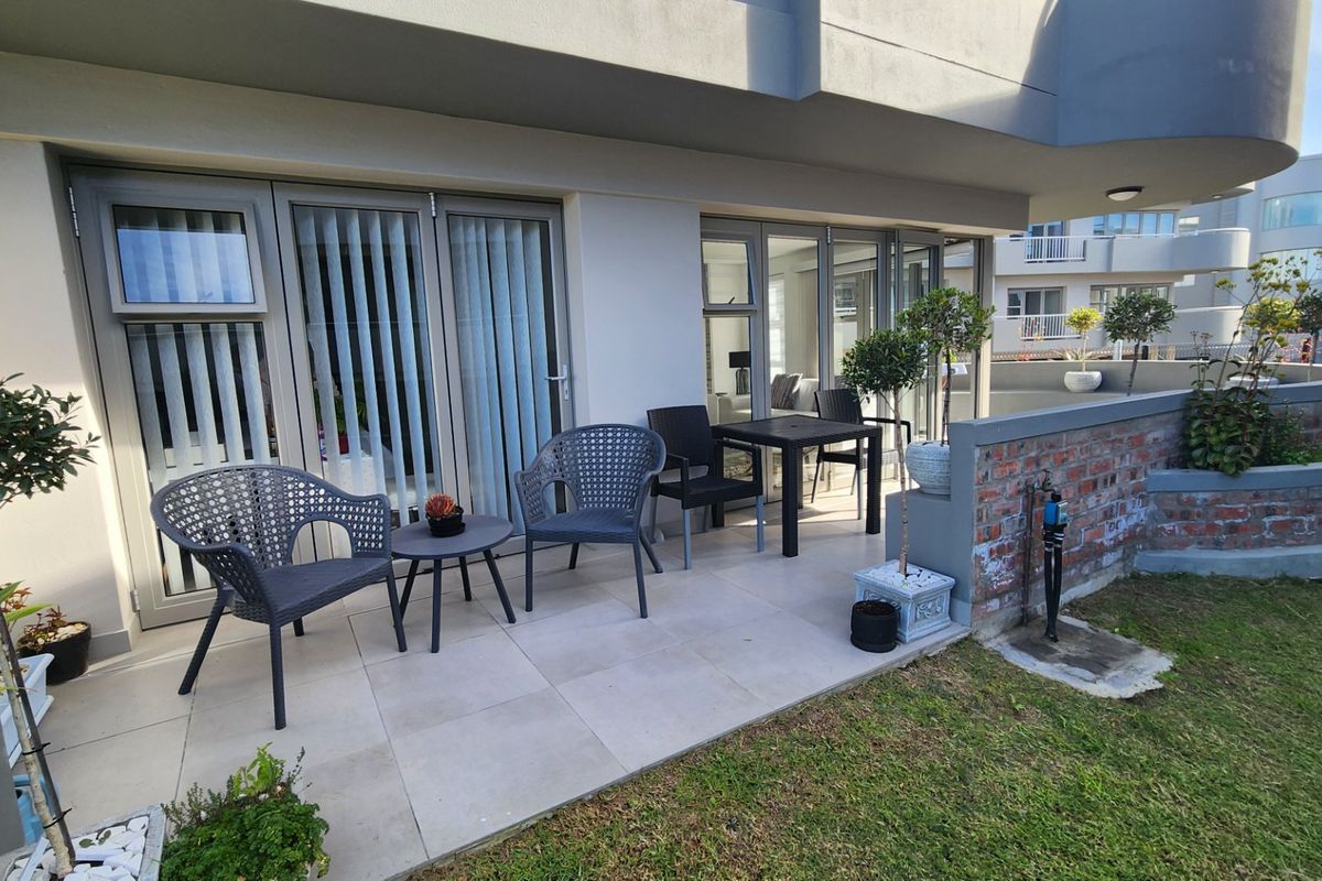 A well-maintained ground floor patio featuring tiled flooring, aluminium sliding doors, and a brick boundary wall, providing a pleasant outdoor seating area.