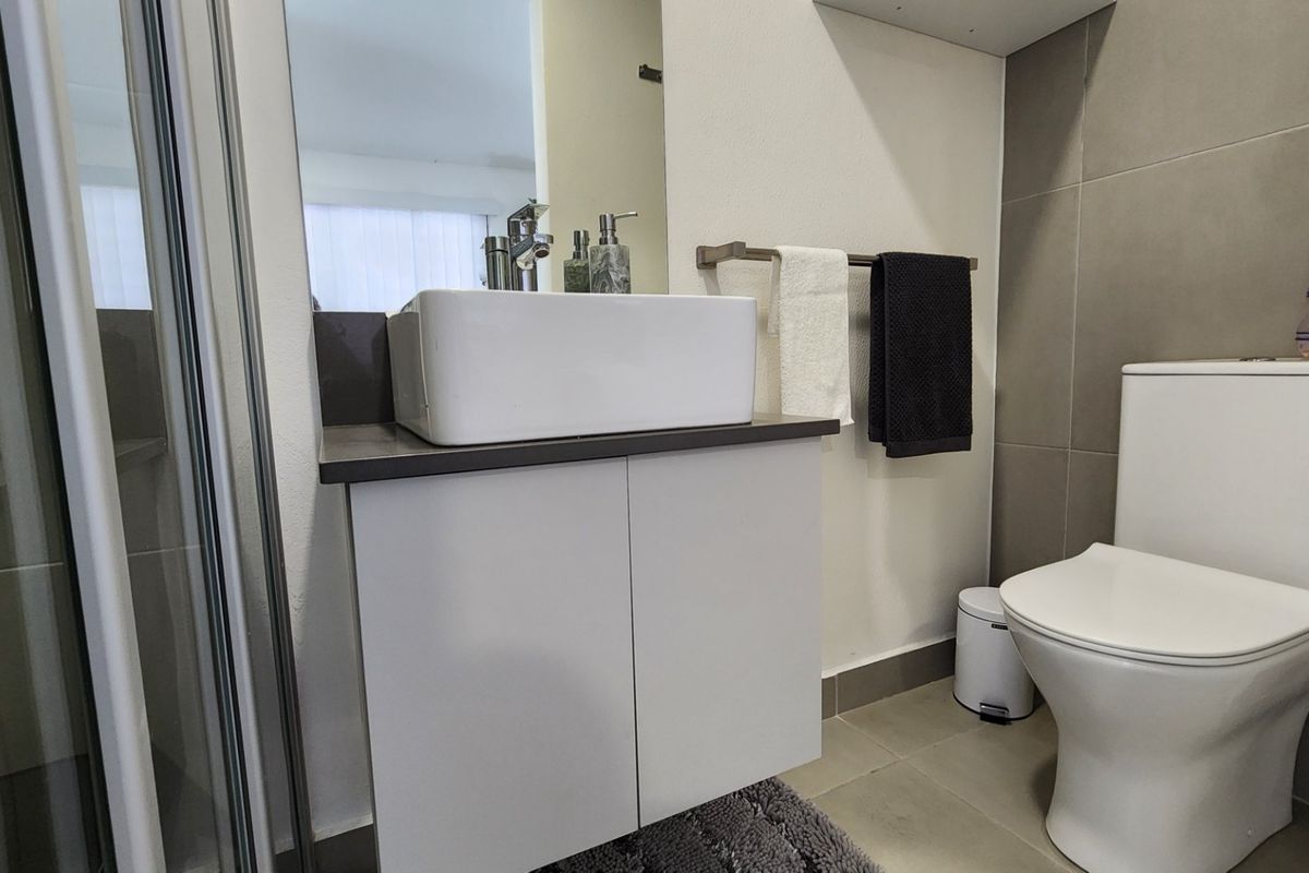 A modern bathroom featuring a vessel sink on a vanity cabinet, a toilet, and a glass-enclosed shower with neutral wall and floor tiling.