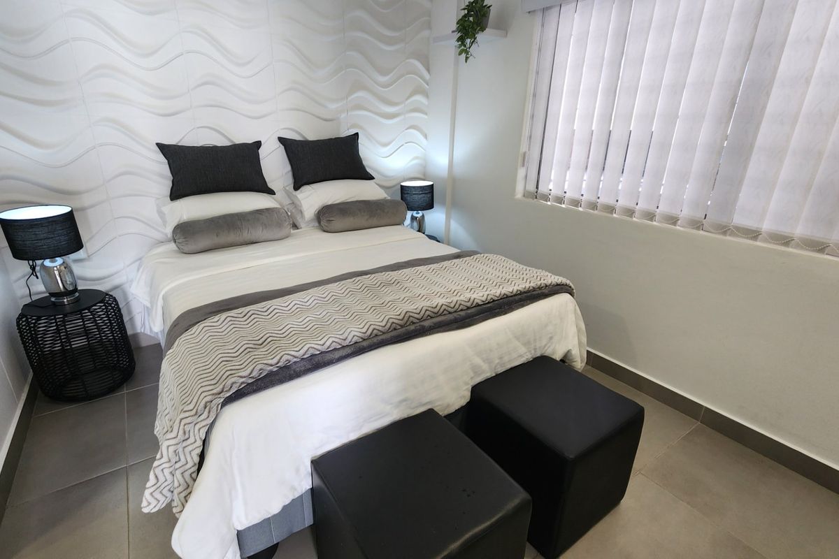 A well-maintained bedroom featuring a modern textured feature wall, neutral tiled flooring, and vertical window blinds for privacy.