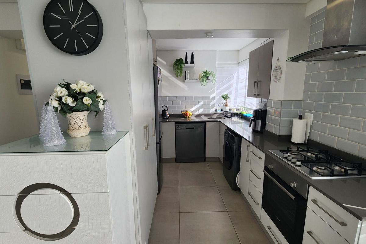 Modern kitchen featuring sleek white cabinetry, stone countertops, subway tile backsplash, and integrated stainless steel appliances including a gas hob and oven.