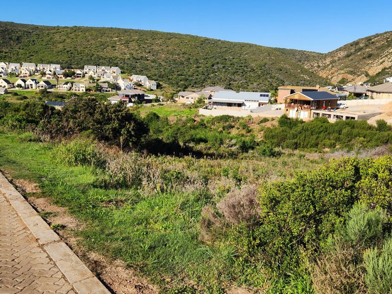 A view of a vacant residential plot overlooking a hillside neighborhood with established homes and natural vegetation.