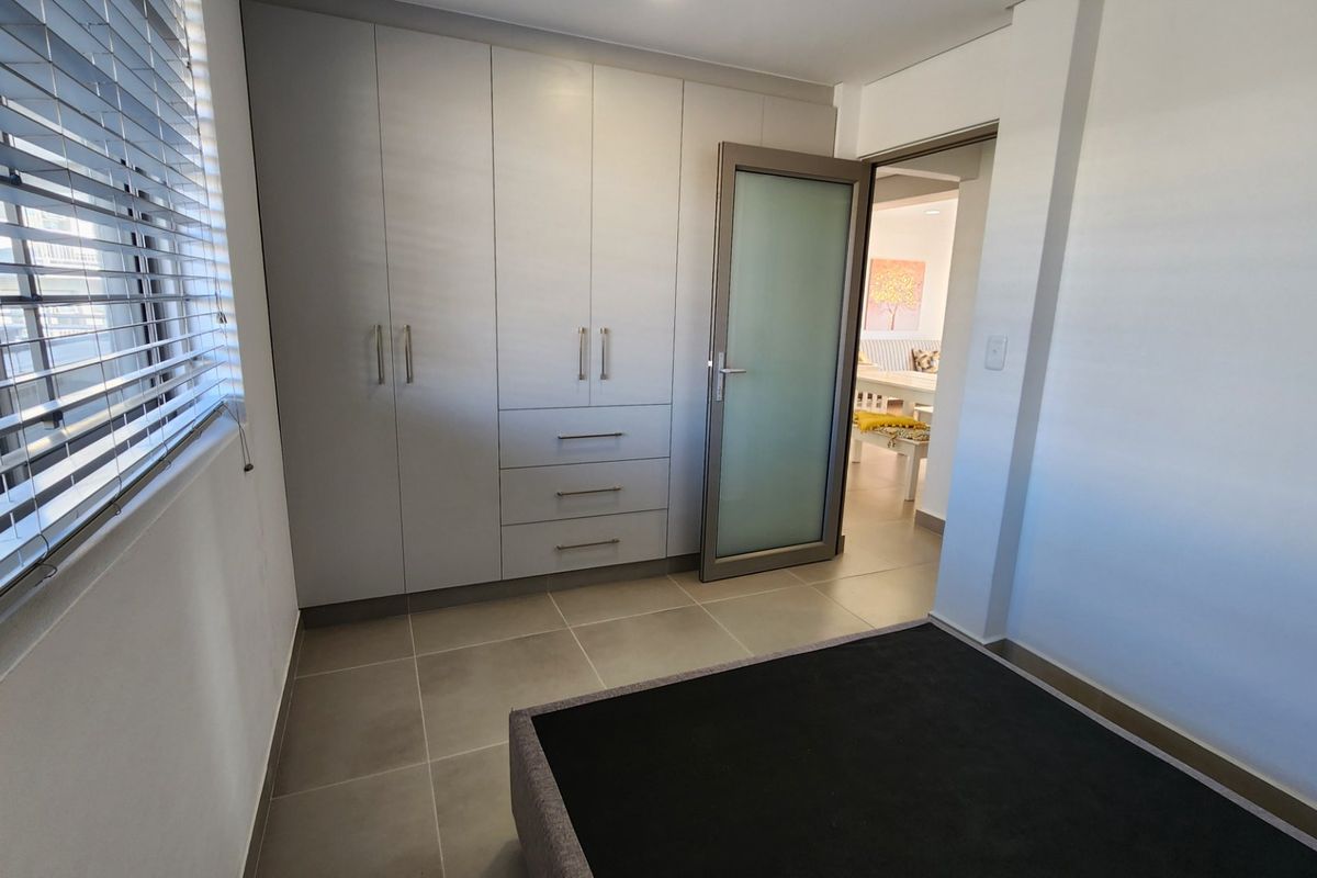 A clean, modern bedroom featuring neutral tiled flooring, ample built-in cupboard storage, and a frosted glass door leading to the living area.