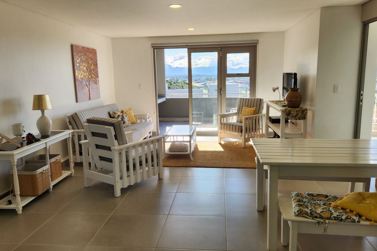 A bright and spacious living area featuring neutral tiled flooring, recessed lighting, and a large sliding glass door leading to an outdoor balcony.