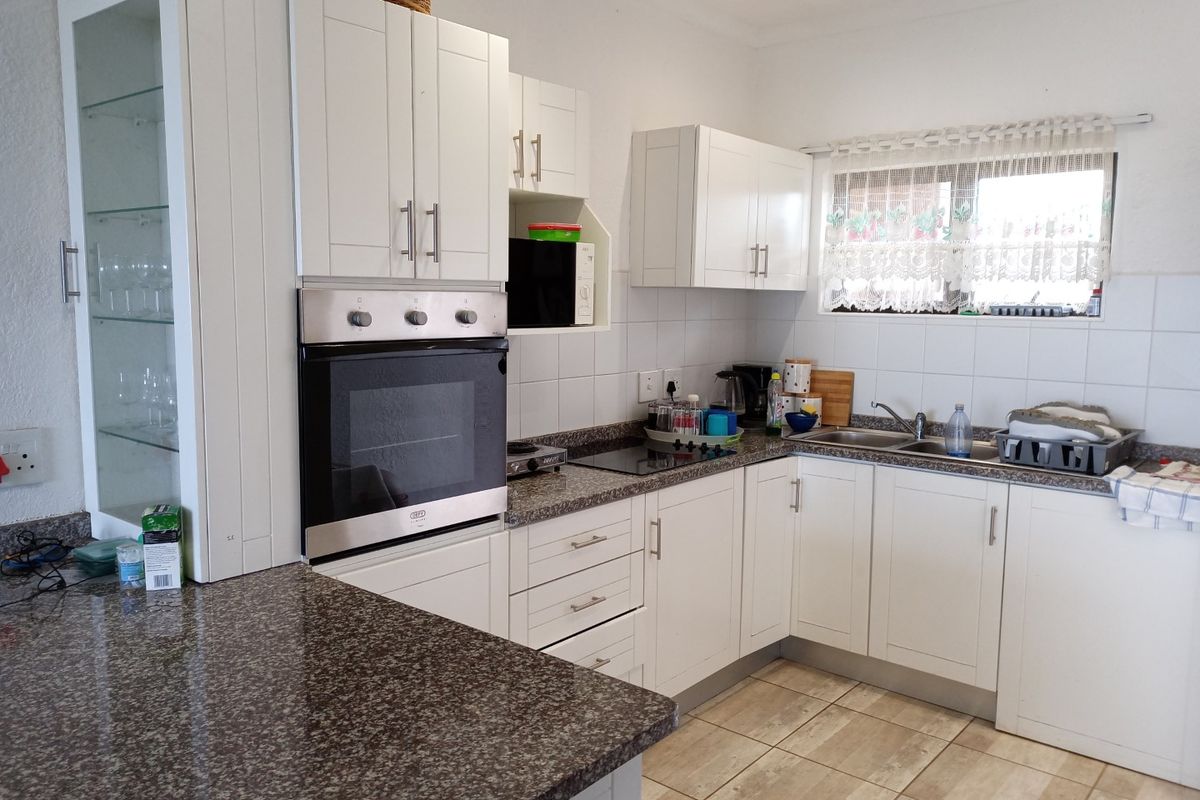 A functional kitchen featuring white cabinetry, granite countertops, a built-in oven, and a tiled backsplash with a window above the sink.